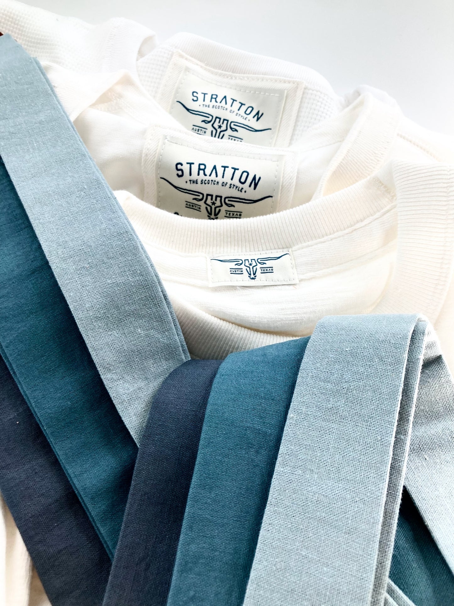 Fine linen button-on suspenders in dusty blue, teal, and slate blue, displayed with Stratton Suspender Co. vintage shirts. Handmade for weddings, groomsmen, and formal menswear. Classic vintage-inspired suspenders with premium craftsmanship.