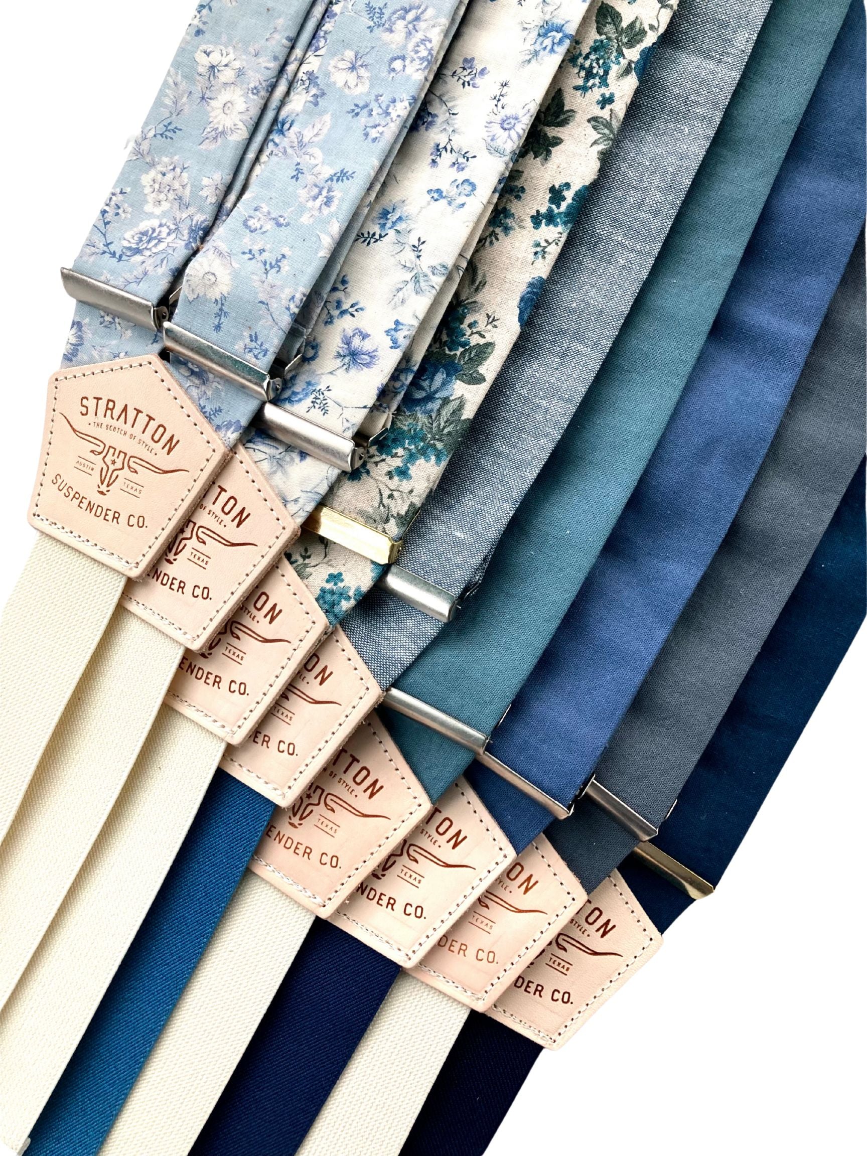 A collection of handmade linen button-on suspenders in powder blue floral, Victorian cornflower blue floral, rustic blue floral, sky blue with ocean blue, teal, French blue with navy, slate blue, and navy with midnight blue. Perfect for weddings, groomsmen, and vintage menswear.