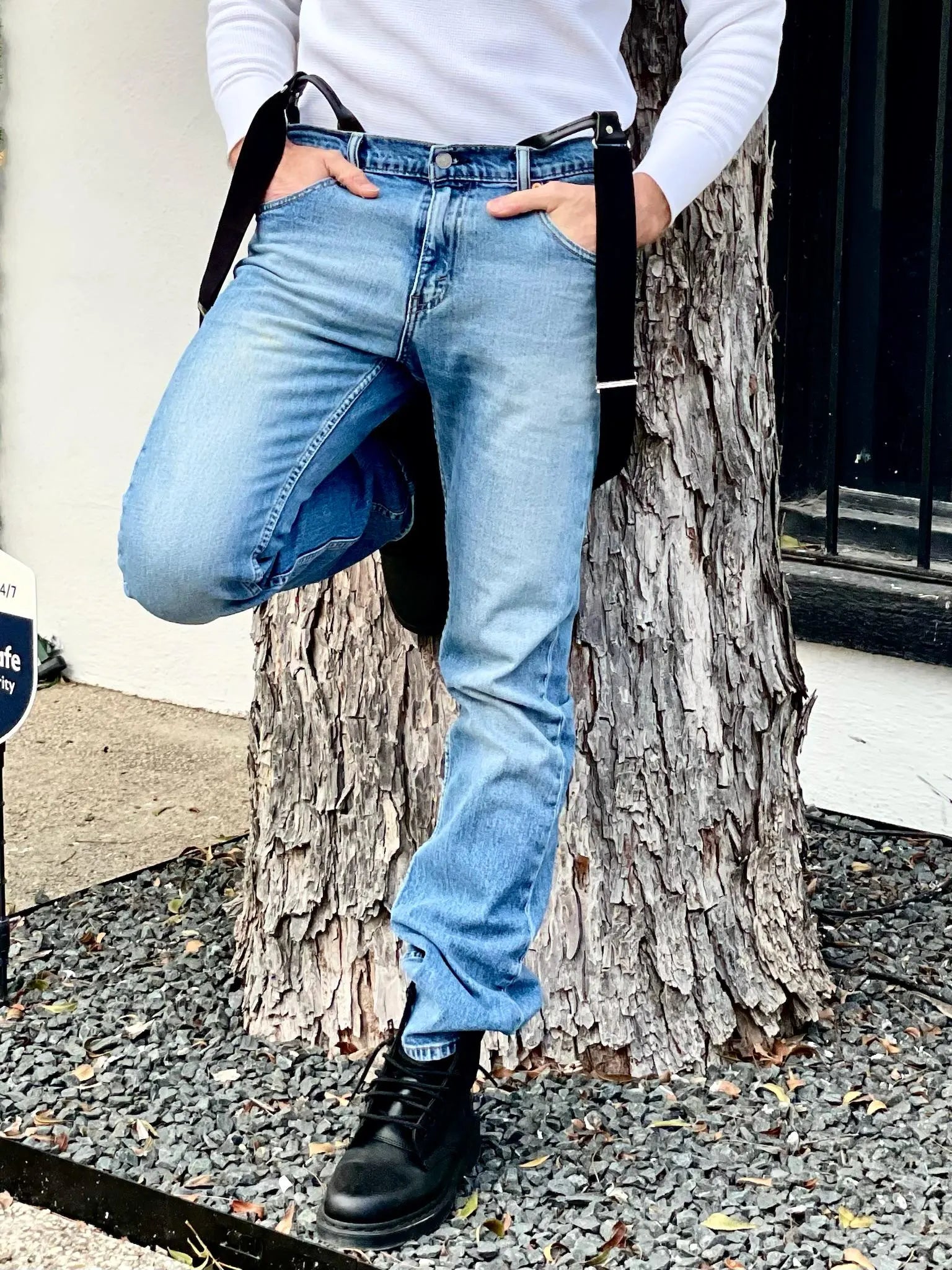 Close-up of black button-on suspenders with silver hardware styled over light wash jeans and a white waffle knit shirt, shown outdoors against a textured tree trunk—handmade men’s suspenders from Stratton Suspender Co. in Austin, Texas.
