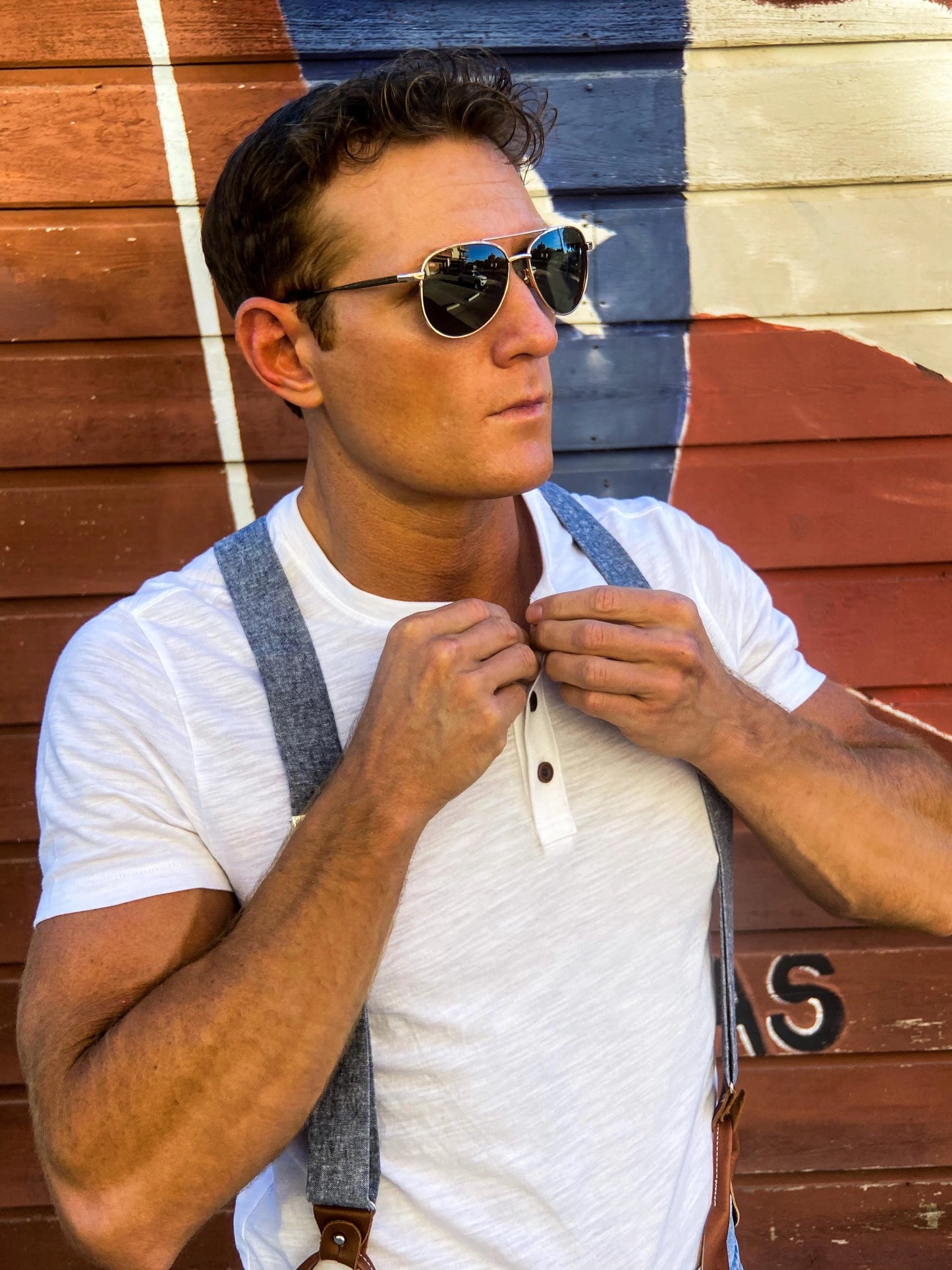 Close-up of a model in leather button-on suspenders and a henley tee adjusting his collar outside the Broken Spoke in Austin, Texas, wearing Stratton Suspender Co. handmade menswear.