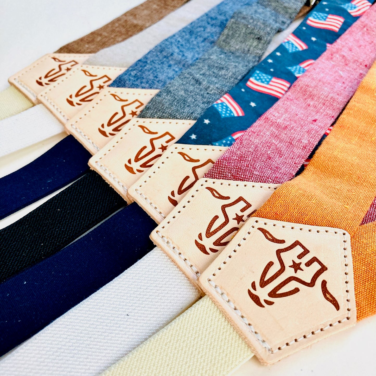 Close-up of children’s magnetic clasp suspenders in assorted colors, featuring linen straps and leather back patches with embossed logo.
