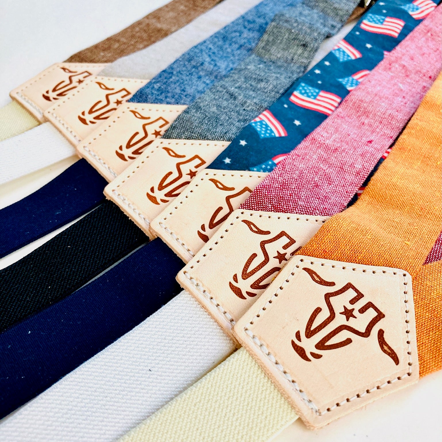 Close-up of children’s magnetic clasp suspenders in assorted colors, featuring linen straps and leather back patches with embossed logo.
