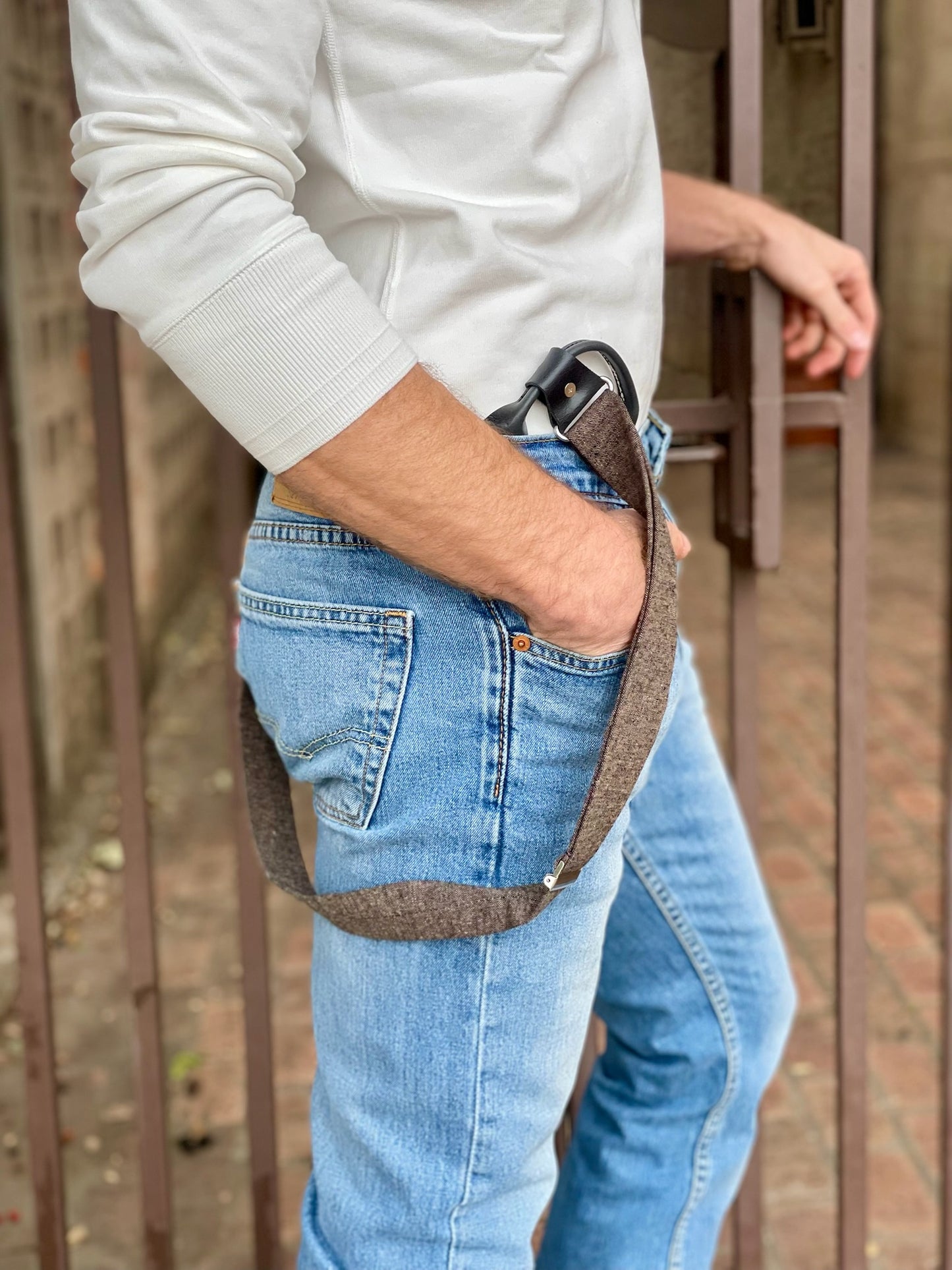 Close-up of handmade espresso brown linen suspenders with black leather button-on attachment, worn with classic denim jeans and ivory Henley, modern rustic menswear style.