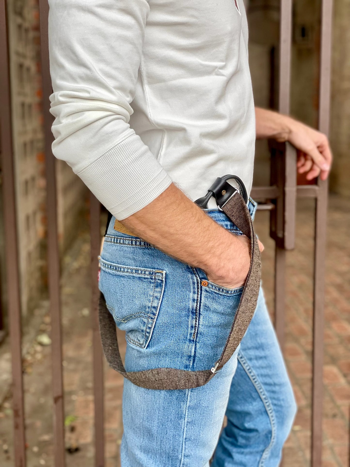 Side view of man wearing espresso brown button-on suspenders with black leather ends, styled with a white Henley and light wash jeans.