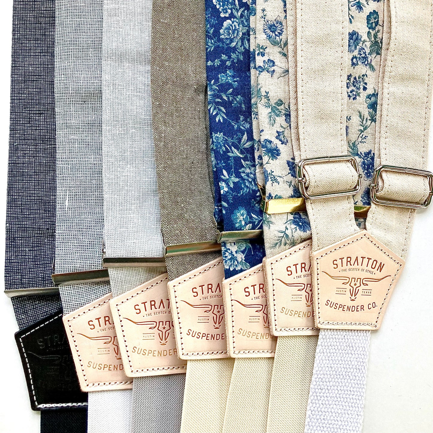 A lineup of handmade linen suspenders in floral and neutral tones, featuring Stratton Suspender Co. leather patches and metal adjusters—perfect for rustic weddings, groomsmen gifts, or heirloom menswear made in Texas.