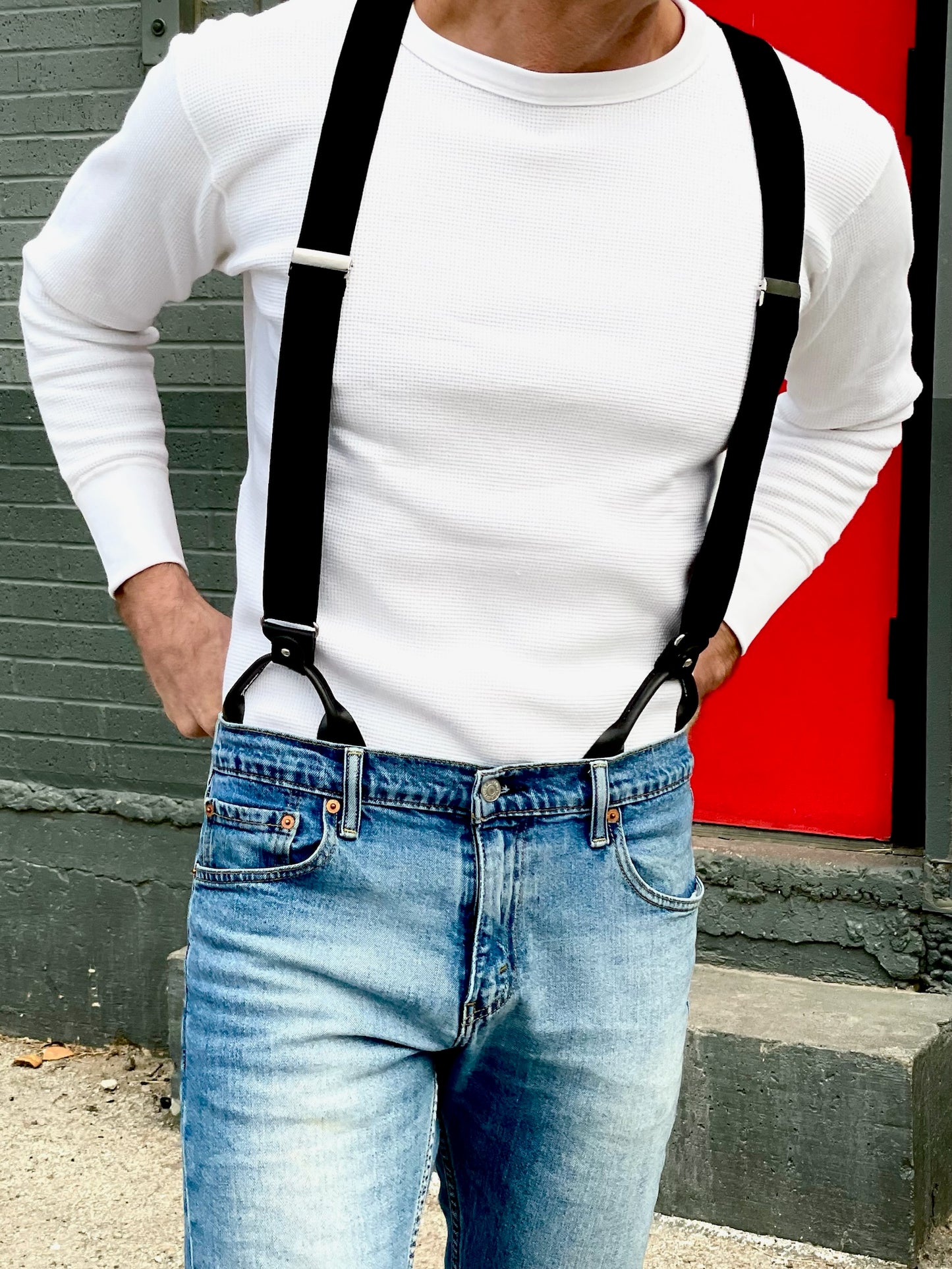 Close-up of man wearing Stratton Suspender Co black button-on suspenders with leather ends over a white waffle-knit shirt and jeans, showing how they attach and fit.