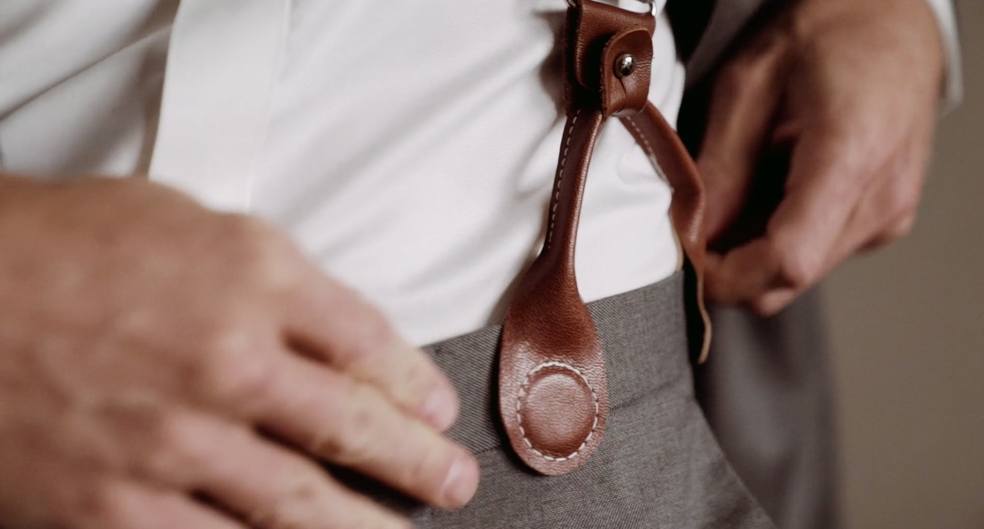 Close-up of leather magnetic suspender clasp—an elegant, clip-free option worn by groomsman at a formal wedding.