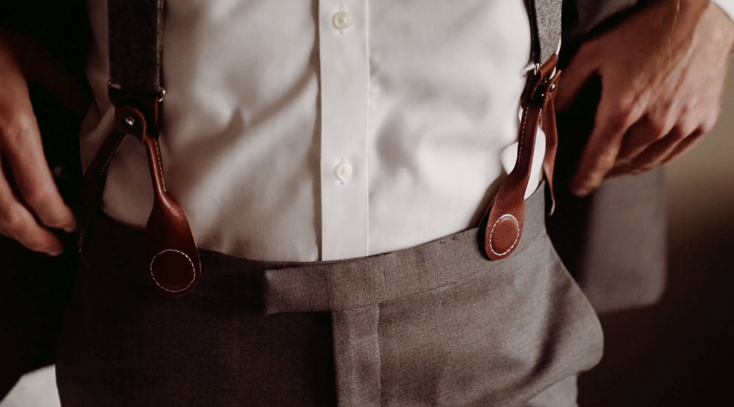 Close-up of leather magnetic clasp suspenders worn by groom with gray suit and white dress shirt. An elegant alternative to clip-on suspenders.