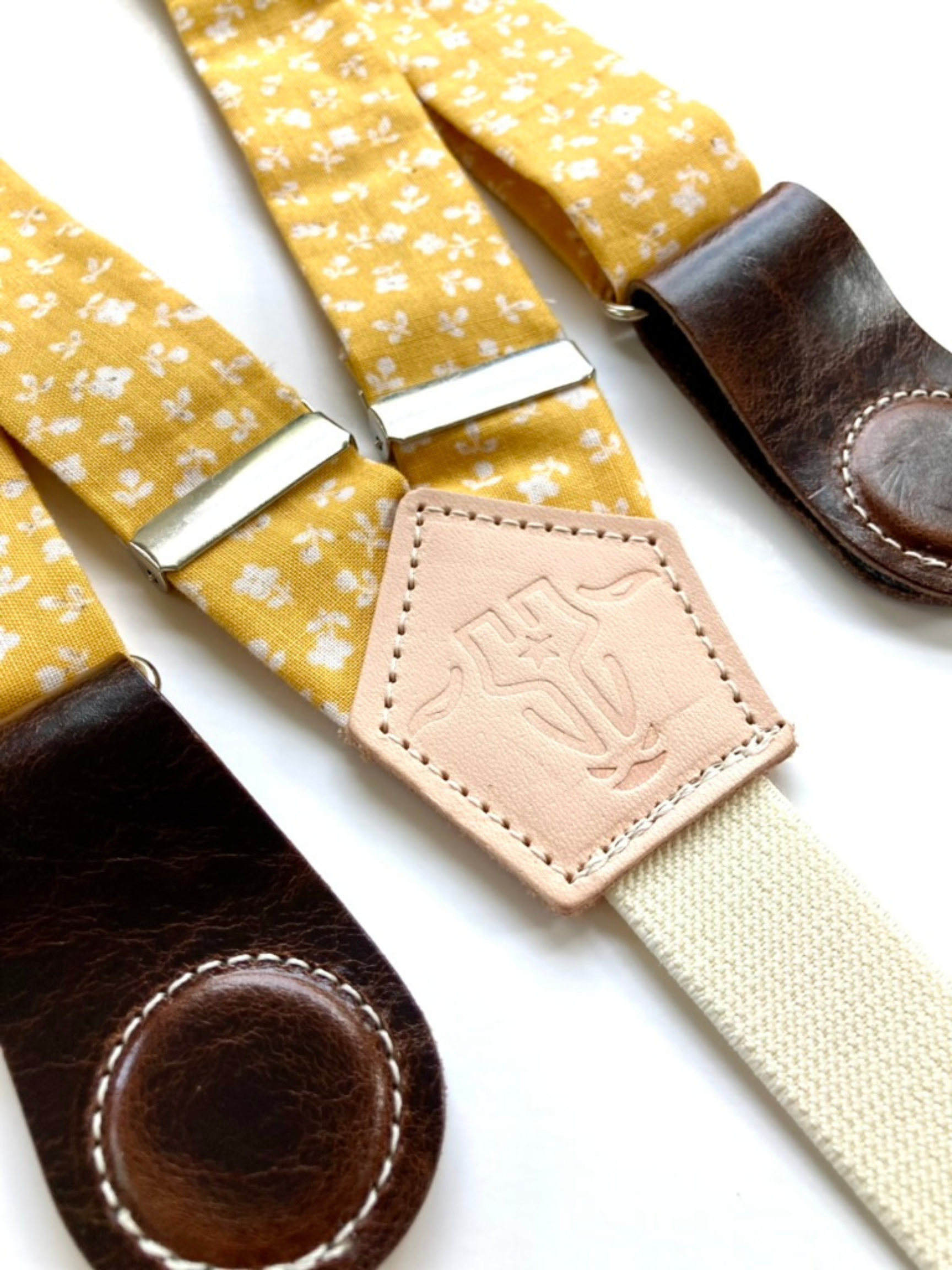 Close-up of marigold floral cotton suspenders with chocolate leather magnetic clasps, vintage-inspired accessory.