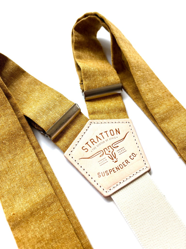 Close-up of marigold yellow rustic wedding suspenders with cream elastic back strap, brushed metal adjusters, and Stratton leather logo patch.