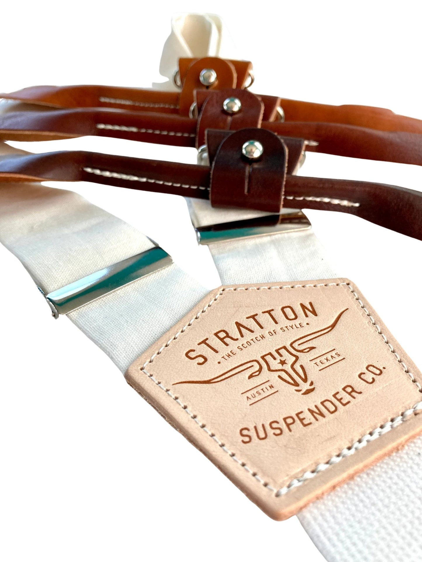 Close-up of pearl white linen suspenders from Stratton Suspender Co. featuring chocolate, cognac, and tan leather button-on ends with polished hardware, ideal for groomsmen or wedding attire.
