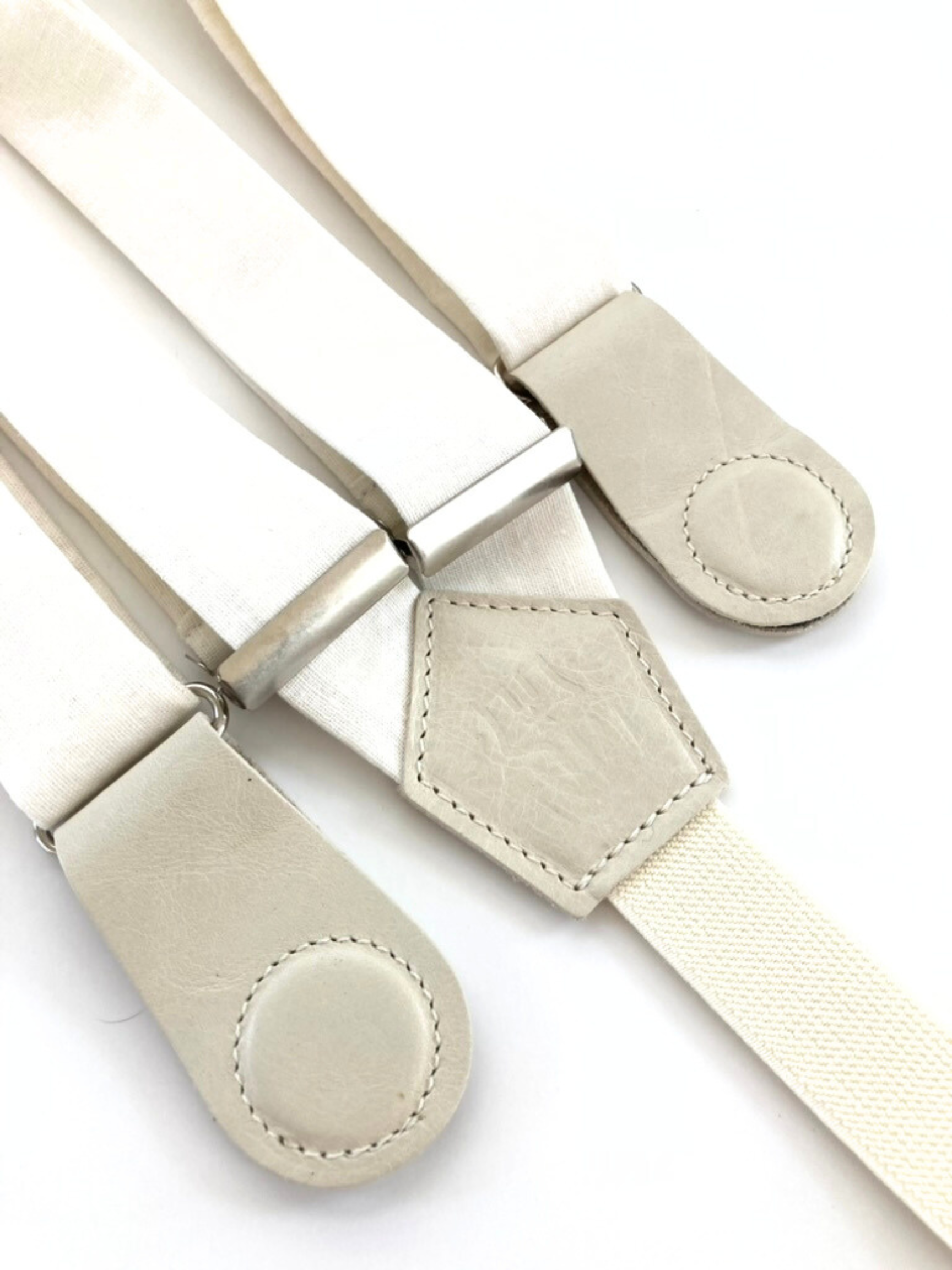 Close-up of pearl white linen suspenders with ivory magnetic leather clasps and silver hardware