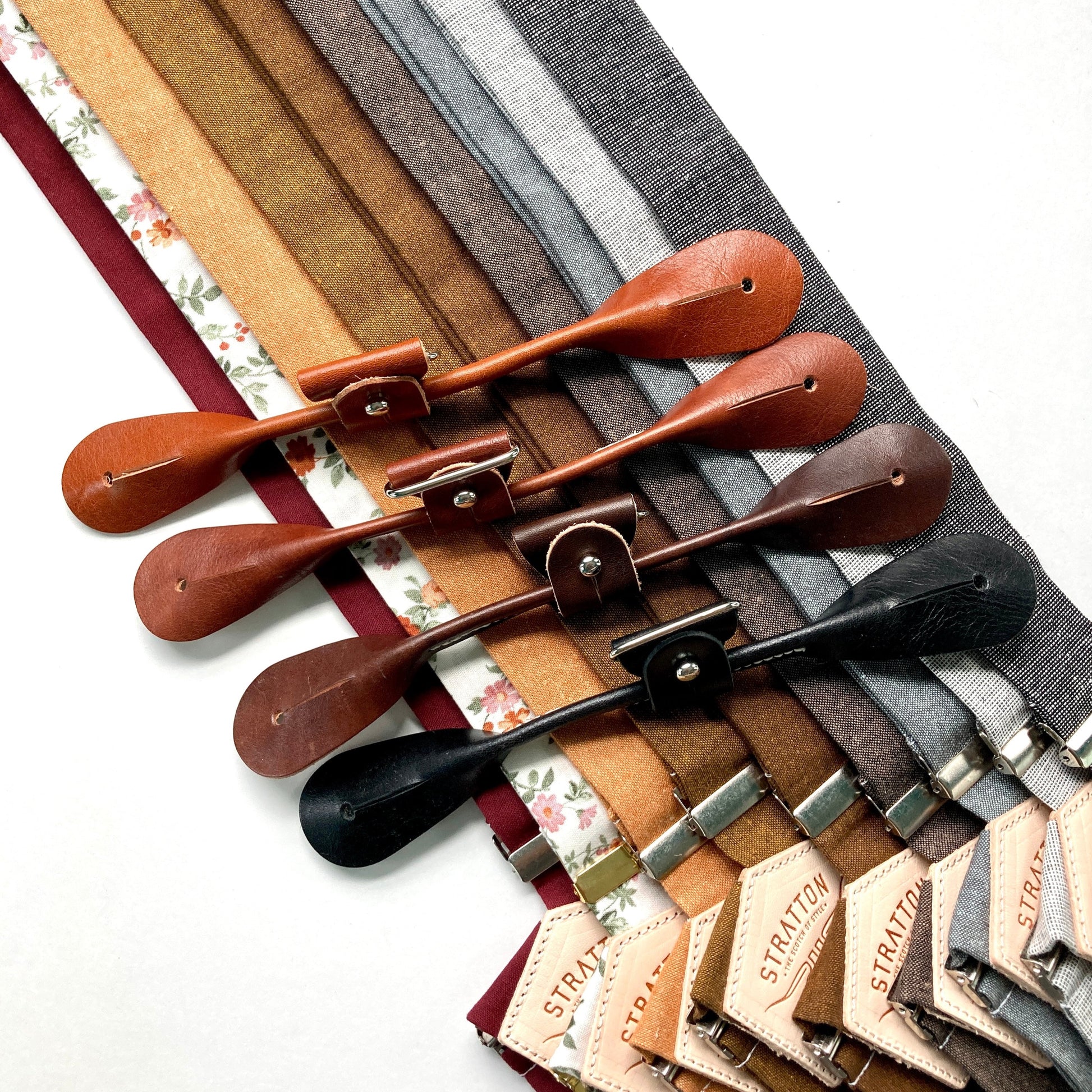 Assorted rustic linen button-on suspenders with full-grain leather attachment tabs in black, brown, and tan, shown in floral, cinnamon brown, mustard, charcoal, and gray tones — ideal for groomsmen, fall weddings, or heritage menswear styling.