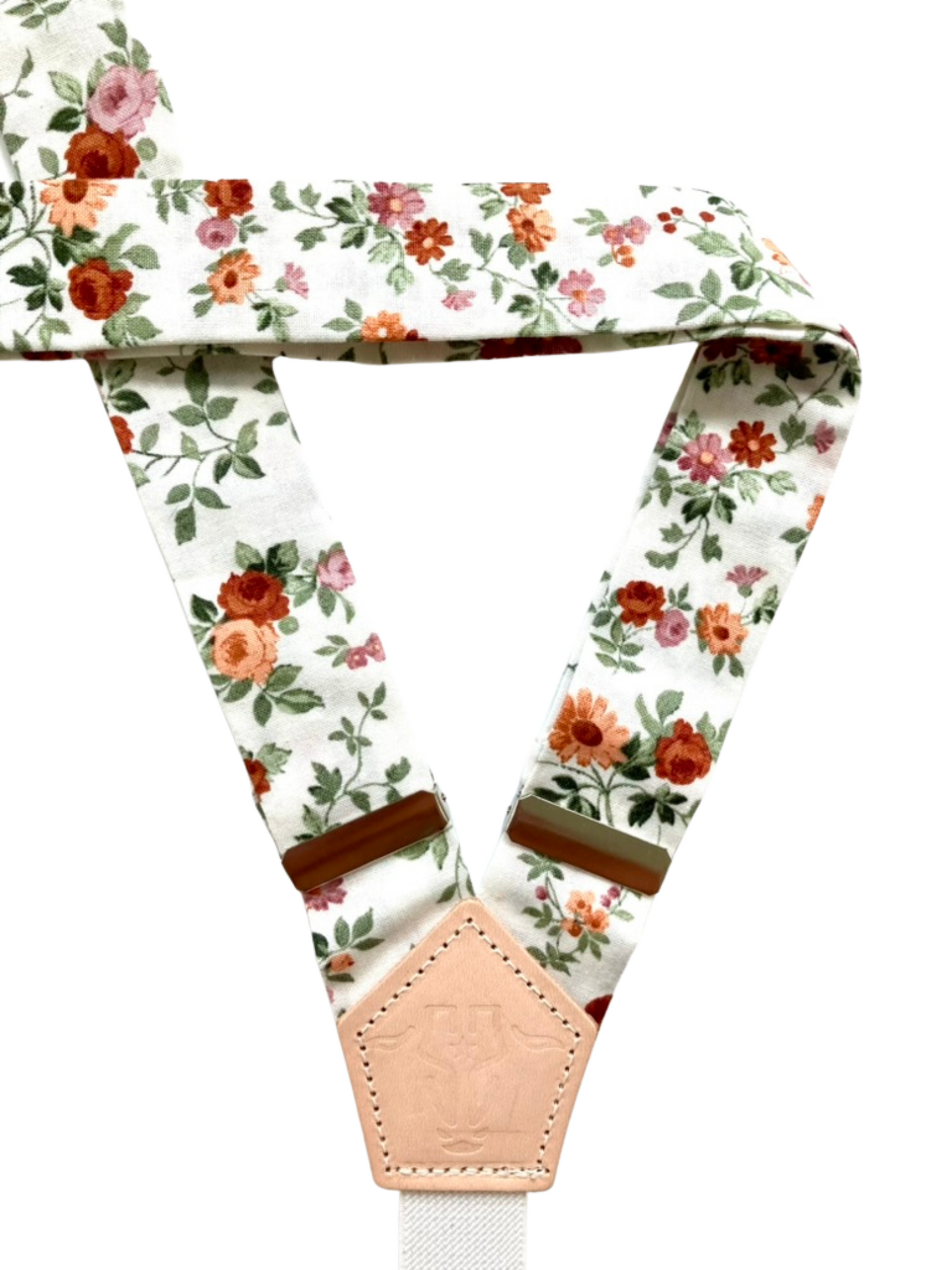 Close-up of floral linen straps and leather back patch on rustic rose women’s suspenders, vintage-inspired accessory.