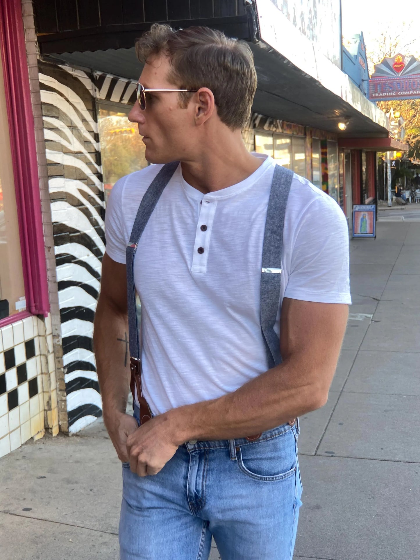 Man wearing Stratton Suspender Co denim blue linen suspenders with leather button-on ends and vintage white henley shirt, walking on South Congress in Austin, Texas.
