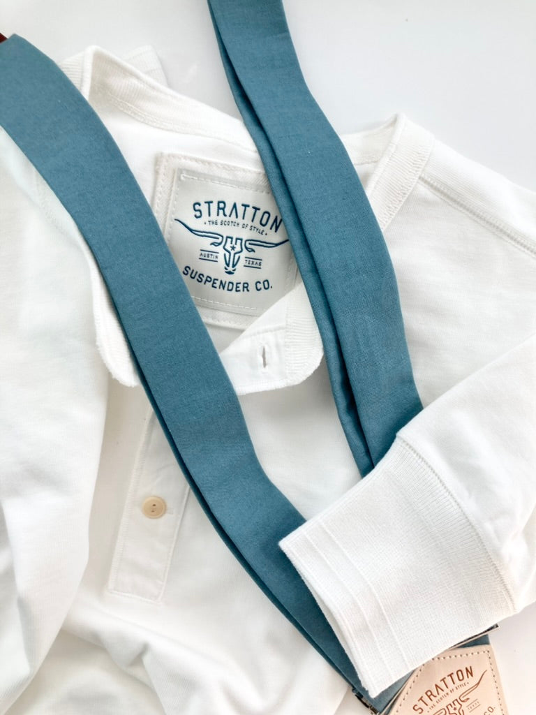 Vintage White Heavyweight Henley by Stratton Suspender Co. styled with blue slate linen suspenders featuring a leather patch and silver hardware. Showcases ribbed cuffs and embroidered brand label, highlighting classic American workwear craftsmanship and heritage-inspired style.
