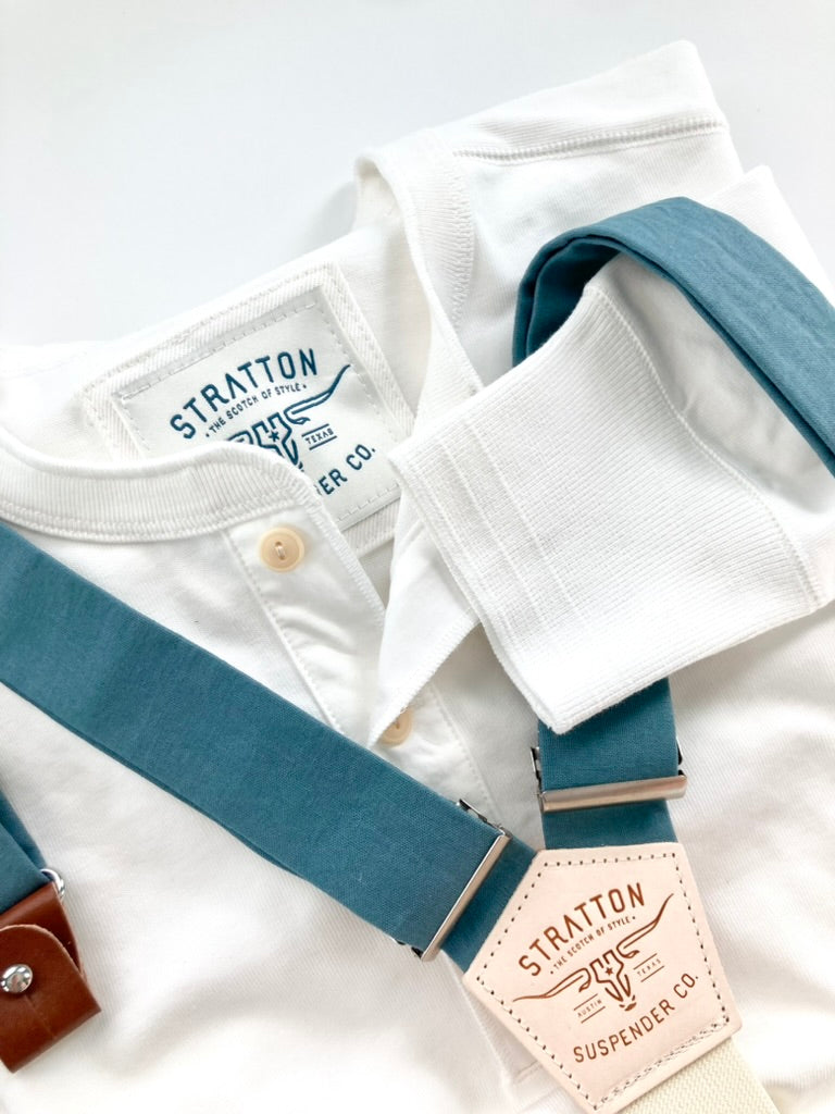 Vintage White Henley by Stratton Suspender Co. styled with blue slate linen suspenders featuring silver adjusters and leather detailing. Showcases ribbed cuffs, heritage branding, and timeless American workwear craftsmanship, perfect for a classic, refined look.