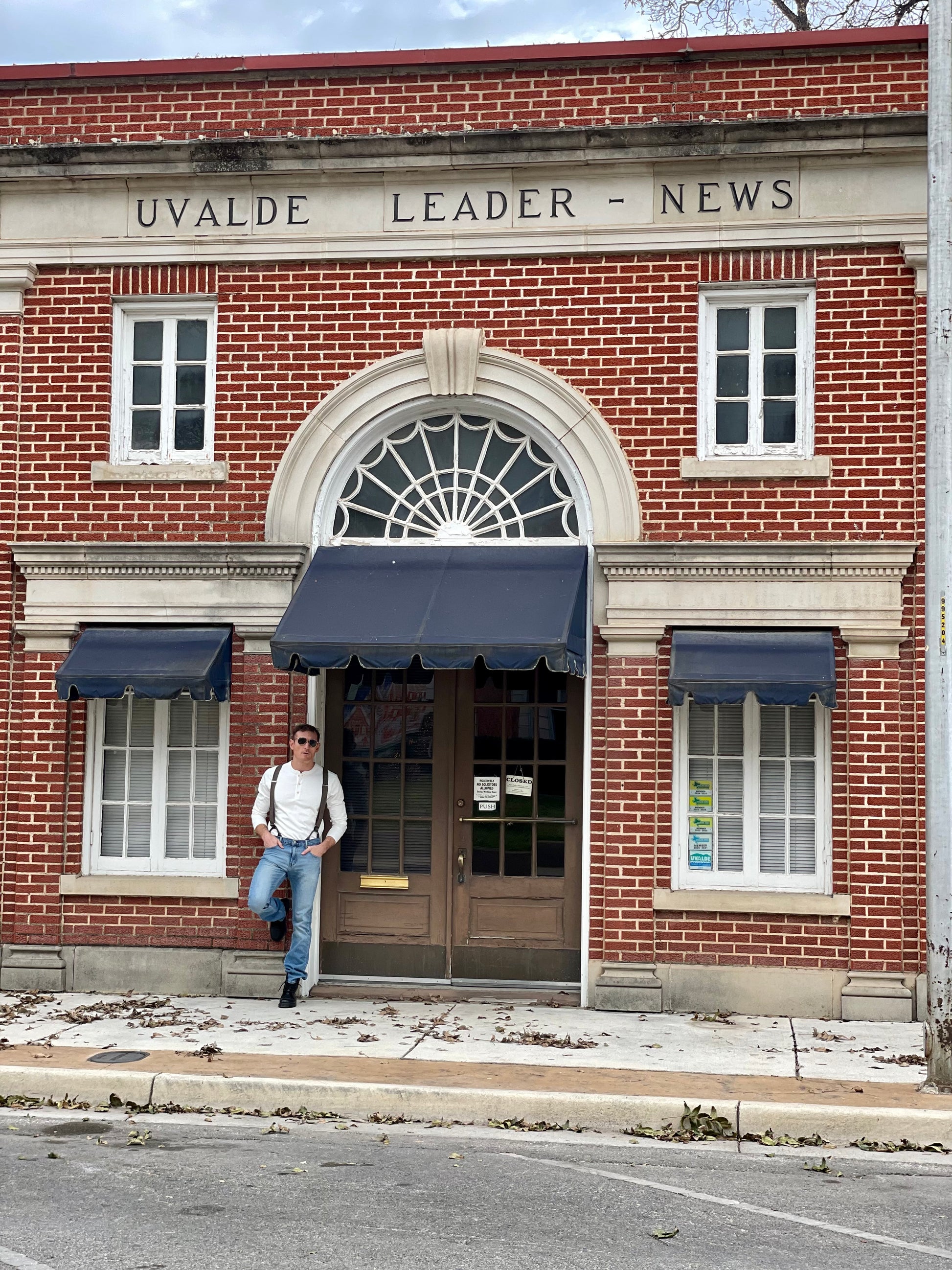 Man wearing a Vintage White Henley and brown wool suspenders by Stratton Suspender Co., standing in front of a historic brick building. Showcasing heritage American workwear, rugged craftsmanship, and timeless menswear style.
