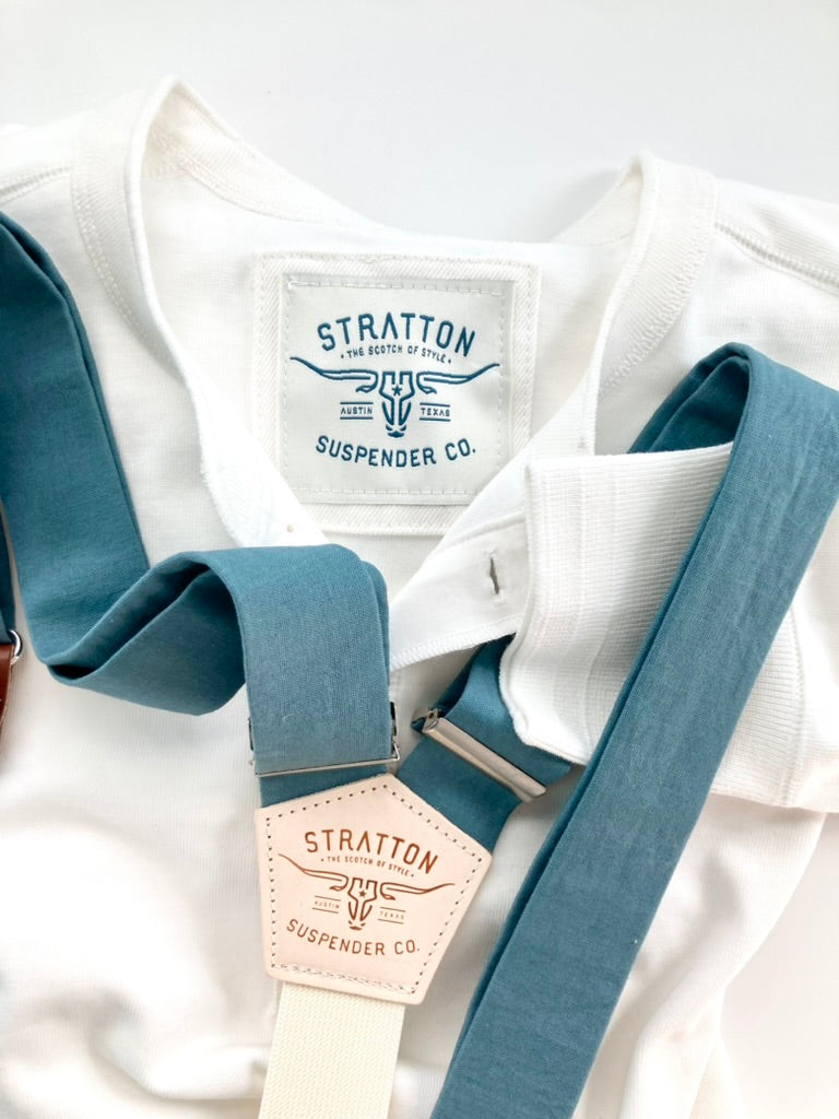 Vintage White Heavyweight Henley by Stratton Suspender Co. paired with slate blue linen suspenders featuring leather patchwork and silver hardware. Showcases embroidered brand label and ribbed cuff. A heritage-inspired American workwear look, crafted for durability and timeless style.