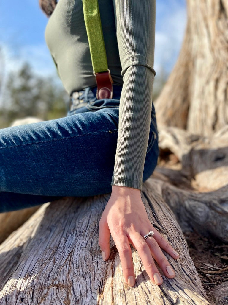 Detail of women’s chartreuse green suspenders styled with high-rise denim and engagement ring—boho fall outfit accessory.