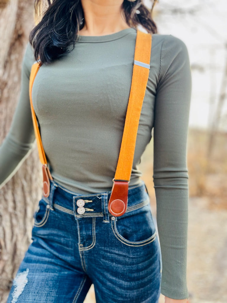 Women’s tangerine orange linen suspenders with tan leather magnetic clasps styled with high-rise denim jeans and fitted long-sleeve top.