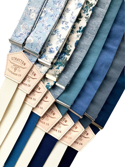 A collection of blue floral and linen suspenders with ivory, navy, and deep blue back straps. Handmade button-on suspenders with premium leather back patches, designed for weddings, groomsmen, and vintage menswear enthusiasts. Timeless, heritage-inspired style with classic craftsmanship.