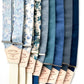A collection of blue linen and floral wedding suspenders with cream and navy elastic back straps. Features premium vegetable-tanned leather back patches. Handmade wedding suspenders, perfect for groomsmen, rustic weddings, and heritage menswear. Ethically crafted for timeless style.