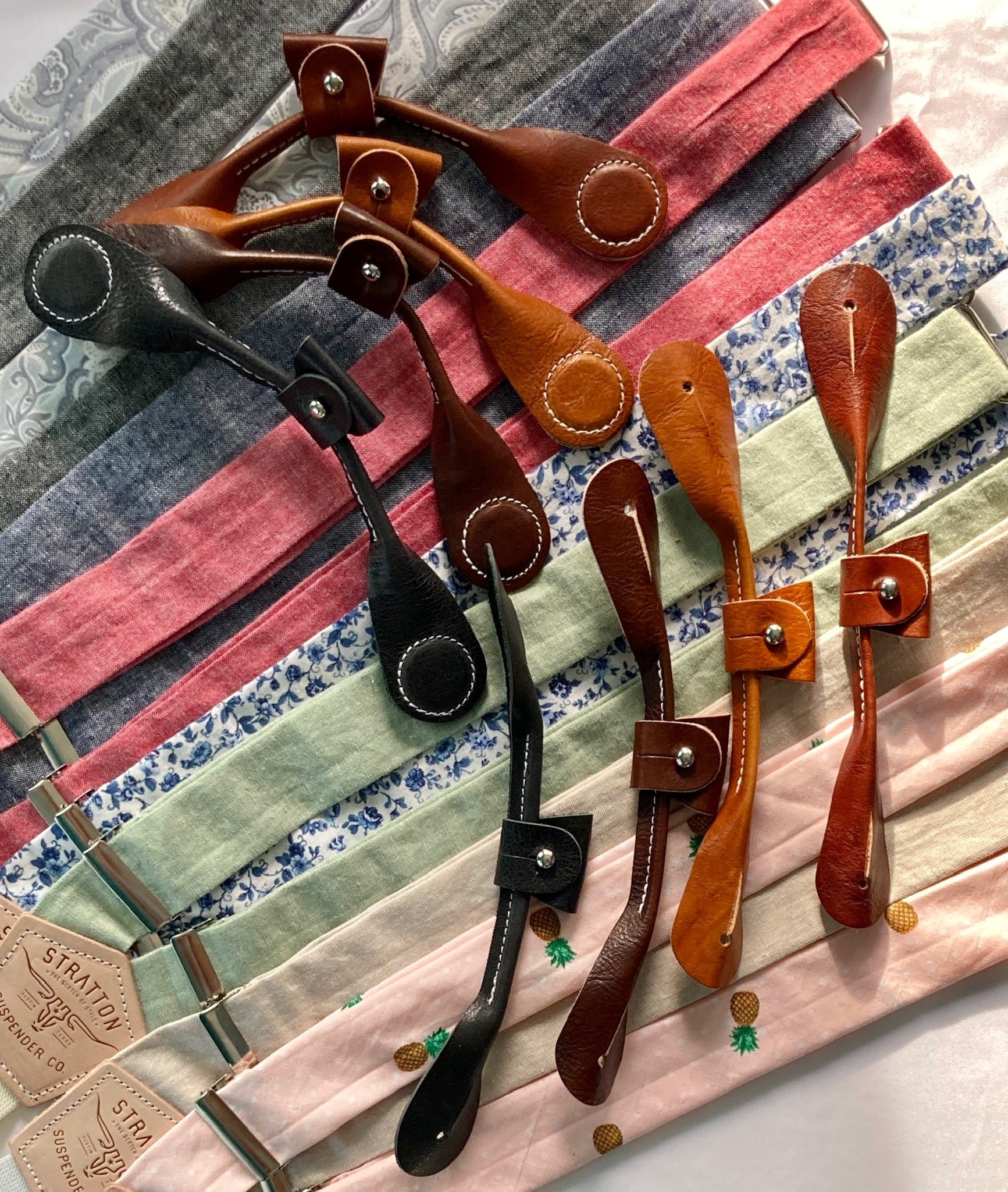 A collection of handmade vintage wedding suspenders in sapphire blue floral, gray paisley, black, navy, cherry red, pistachio green, beige, and pastel pink. Features full-grain veg-tan leather button-on and magnetic clasp attachments in cognac, tan, chocolate, and black. Designed for grooms, groomsmen, and classic menswear enthusiasts, these suspenders offer heritage craftsmanship with modern versatility—perfect for formal events, rustic weddings, and timeless styling.