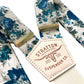 Close-up of Heritage Blue Floral Linen Suspenders with a premium veg-tan leather back patch and handcrafted button-on leather attachments in black, chocolate, cognac, and tan. Designed for weddings, groomsmen, and vintage menswear. Ethically handmade by Stratton Suspender Co.