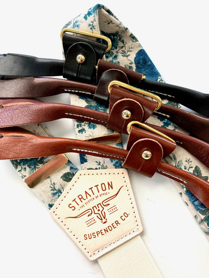 Close-up of heritage blue floral linen suspenders with a cream elastic back strap and premium leather button-on attachments in black, chocolate, cognac, and tan. Handmade wedding suspenders, perfect for grooms, groomsmen, and vintage menswear. Ethically crafted for timeless style.