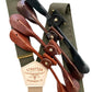 Close-up of olive green linen suspenders with a taupe back strap, brass hardware, and interchangeable full-grain leather button attachments in black, chocolate, cognac, and tan. A premium accessory for weddings, groomsmen, and heirloom menswear.