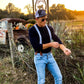 A groom styling Sapphire Blue Floral wedding suspenders with a navy blue Henley shirt and light-wash jeans at a rustic Texas wedding. These button-on suspenders feature a vintage-inspired blue floral pattern on linen straps, full-grain leather button-on attachments, and polished brass hardware. Designed for grooms, groomsmen, and rustic wedding themes, offering a refined, tailored look superior to clip-ons. Perfect for country weddings, vintage menswear, and heritage-inspired formalwear.