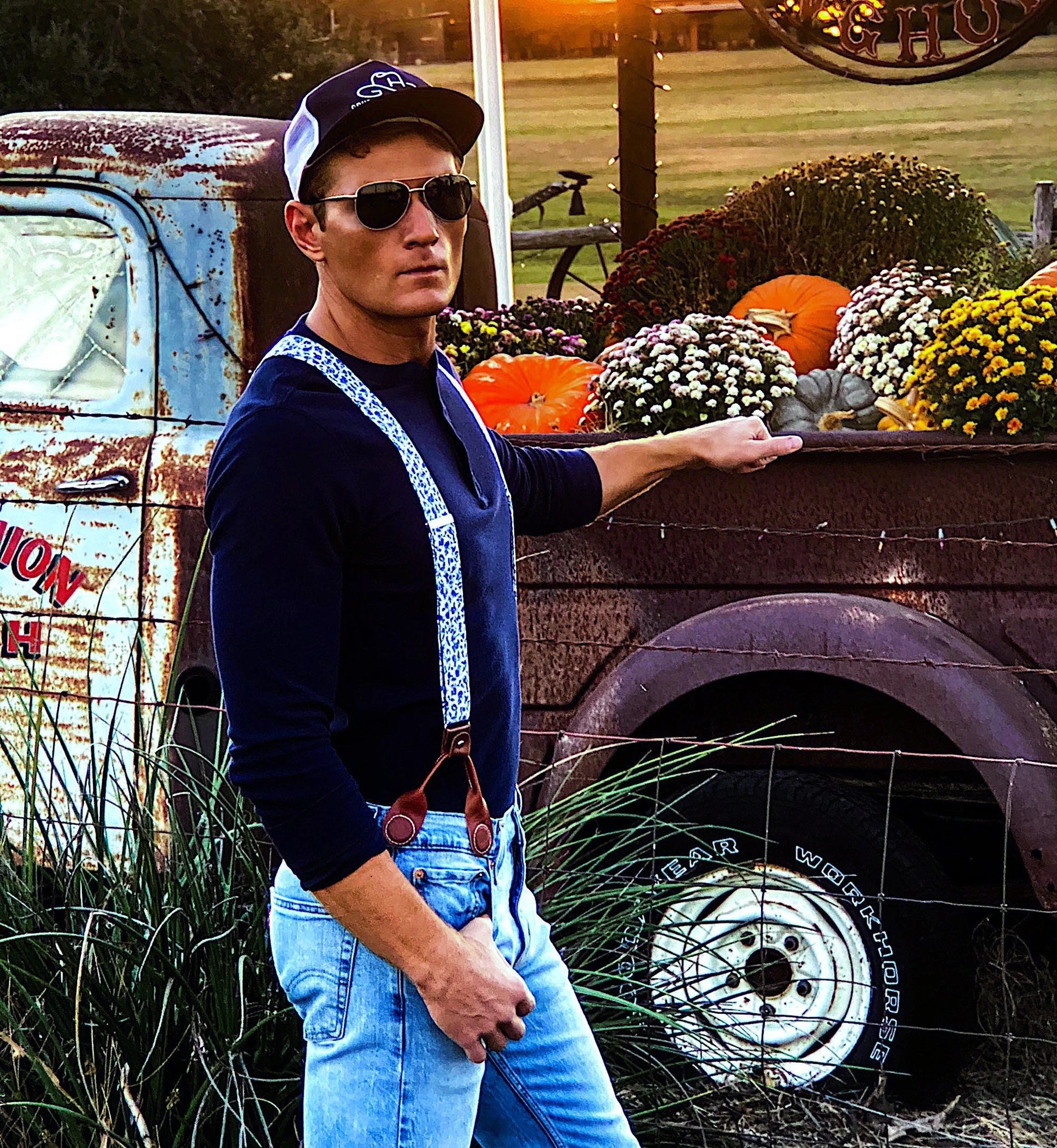 A groom wearing Sapphire Blue Floral wedding suspenders at a rustic Texas wedding, styled with a navy Henley shirt and light-wash denim. These vintage button-on suspenders feature a blue floral linen strap, white elastic back, and full-grain leather button-on attachments for a tailored, heritage menswear look. Designed for grooms, groomsmen, and rustic wedding themes, offering a superior alternative to clip-on suspenders. Ideal for Western weddings, farmhouse wedding styles, and country-chic groom attire.