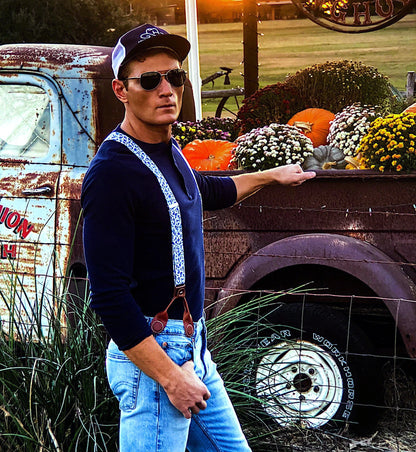 A groom wearing Sapphire Blue Floral wedding suspenders at a rustic Texas wedding, styled with a navy Henley shirt and light-wash denim. These vintage button-on suspenders feature a blue floral linen strap, white elastic back, and full-grain leather button-on attachments for a tailored, heritage menswear look. Designed for grooms, groomsmen, and rustic wedding themes, offering a superior alternative to clip-on suspenders. Ideal for Western weddings, farmhouse wedding styles, and country-chic groom attire.