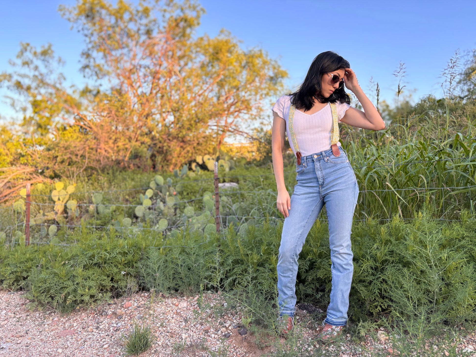 Floral women’s magnetic clasp suspenders with leather attachments, worn with blue jeans and a white knit top outdoors.