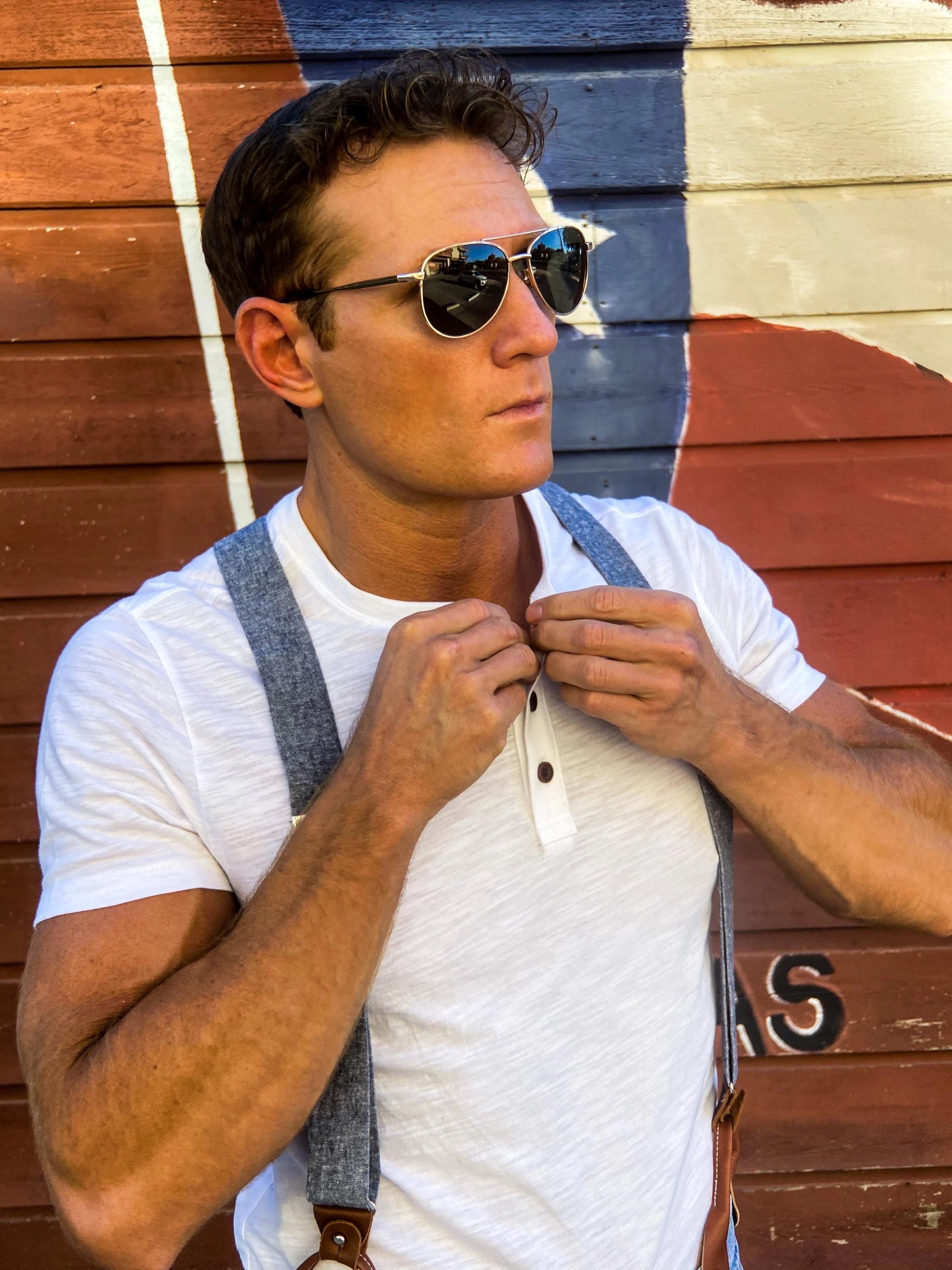 Close-up of a model in leather button-on suspenders and a henley tee adjusting his collar outside the Broken Spoke in Austin, Texas, wearing Stratton Suspender Co. handmade menswear.