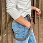 Close-up of brown linen button-on suspenders with black leather tabs, draped at the side of light-wash jeans and paired with a cream shirt, handmade in Texas by Stratton Suspender Co. for groomsmen, rustic weddings, and vintage men’s fashion.
