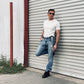 Man wearing charcoal and beige woven button-on suspenders from Stratton Suspender Co., styled with light wash jeans, black boots, and a fitted white tee—handmade in Texas for rustic weddings, groomsmen gifts, and heritage menswear.