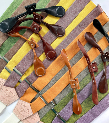 A vibrant assortment of handmade linen button-on suspenders in mustard, sage, lavender, brown, and charcoal hues, each with genuine leather tabs and metal hardware, designed by Stratton Suspender Co. for rustic weddings, groomsmen, and heirloom-quality menswear.