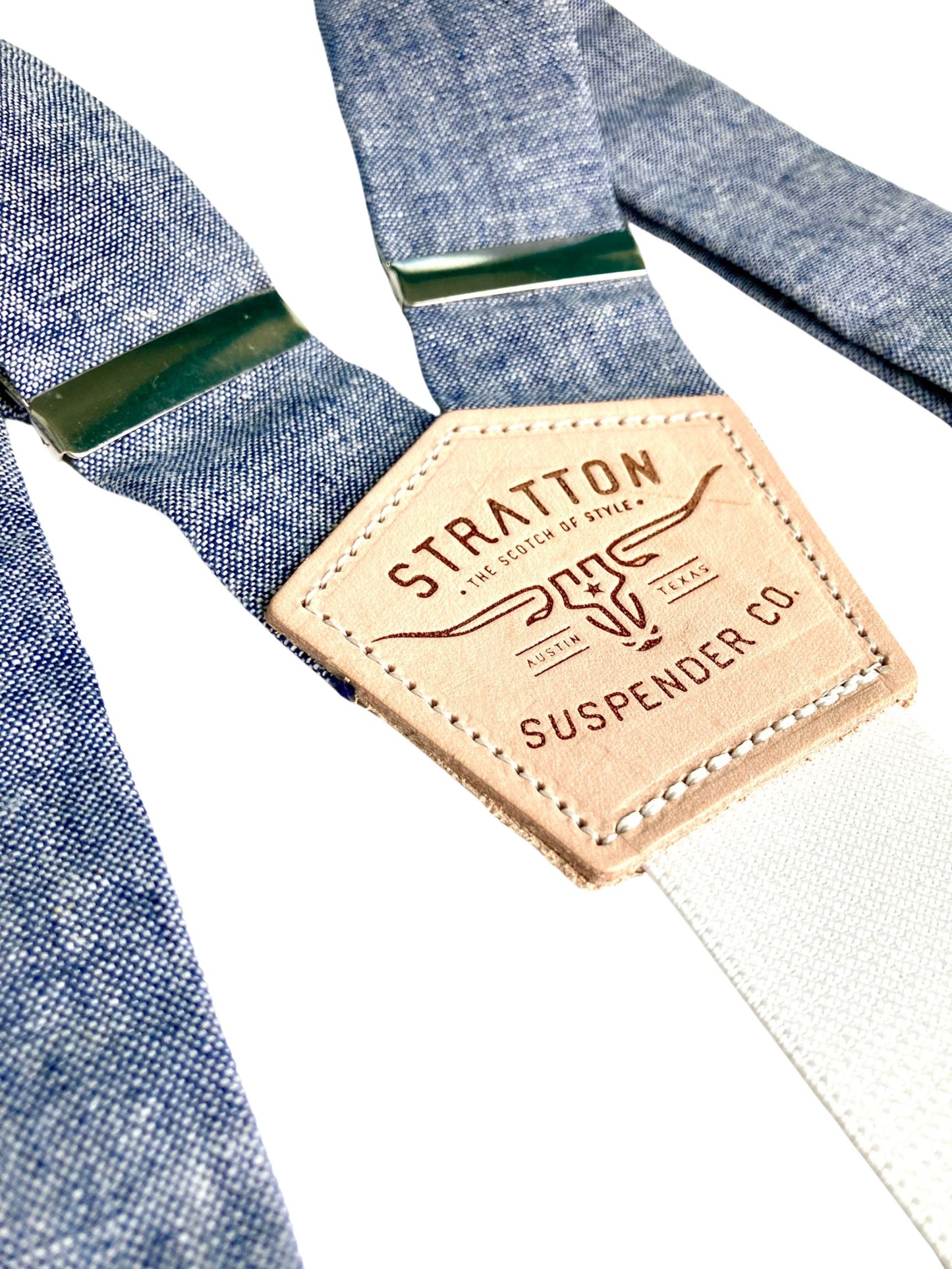 Close-up of Stratton Suspender Co.’s denim blue linen suspender straps with premium vegetable-tanned leather detailing. Featuring silver adjusters and a vintage-inspired leather patch, these handmade suspenders offer a refined alternative to clip-ons, ideal for weddings and formalwear.