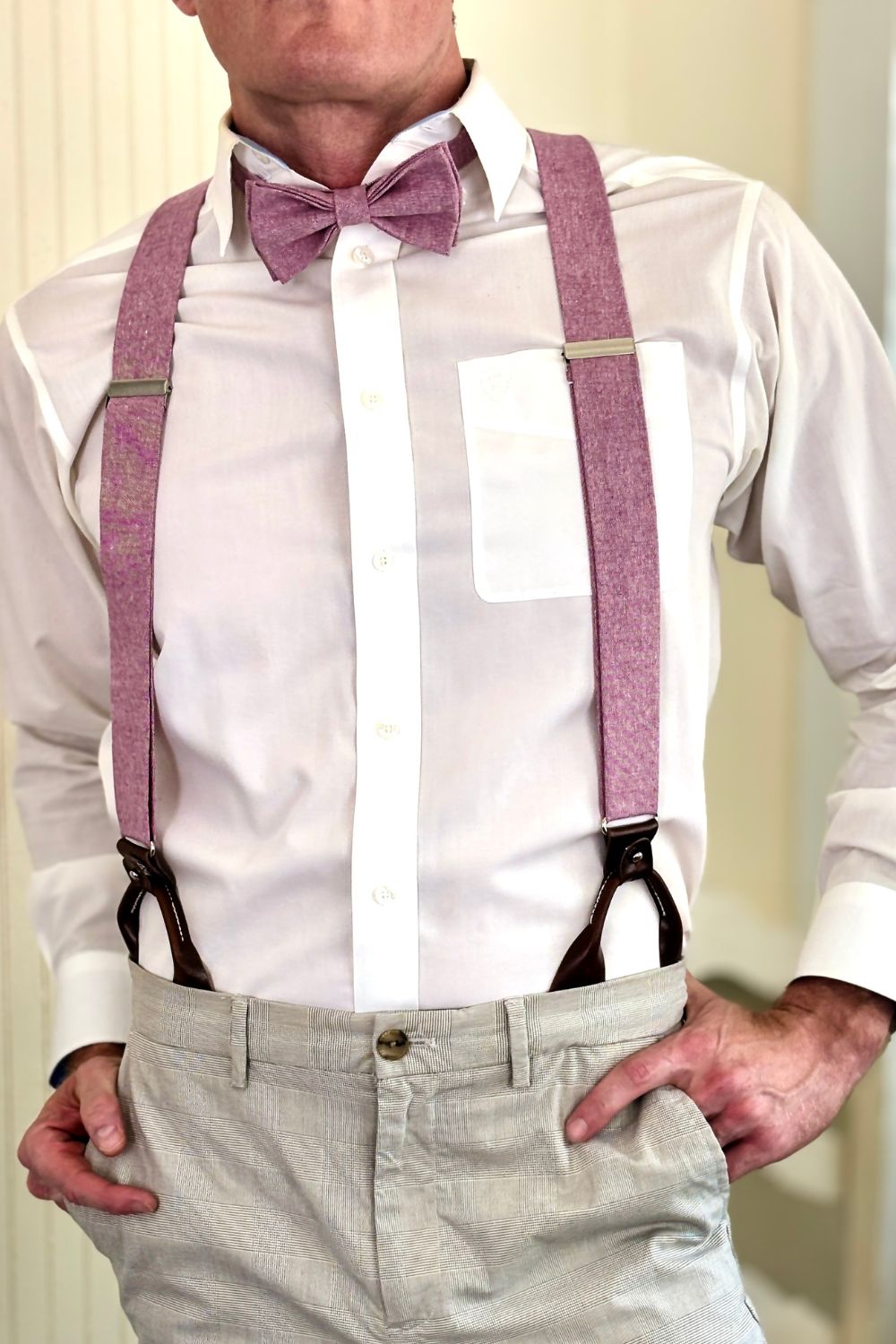 Person wearing a white shirt, light gray pants, and pink suspenders with a bow tie.