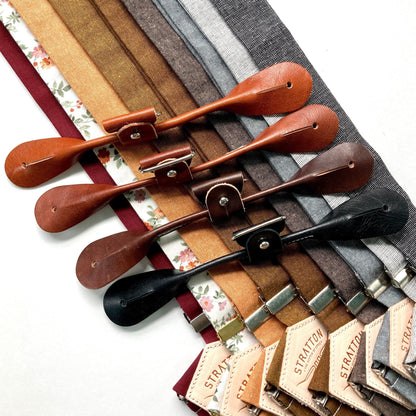 A variety of handmade button-on suspenders from Stratton Suspender Co. in rich fall tones—burgundy, floral, pecan, espresso, charcoal, and black—with matching leather button attachments, ideal for rustic weddings and groomsmen attire.