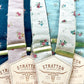 Lineup of Stratton Suspender Co. handmade floral linen suspenders in blush, navy, ivory, and powder blue with gold adjusters and tan leather back patches, perfect for weddings and groomsmen.