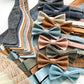 Flat lay of handmade linen bow ties with matching suspenders in earthy and pastel tones—ideal for rustic weddings, groomsmen gifts, and men’s formalwear. Includes self-tie and pre-tied options by Stratton Suspender Co.