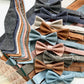 Flat lay of handmade bow ties and matching linen suspenders in neutral, earth, and pastel tones — a coordinated set for groomsmen or vintage-inspired menswear.