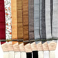 Assorted linen button-on suspenders in a range of solid, floral, and earth-tone fabrics with leather back patches, handmade in Texas for grooms, groomsmen, and heritage formalwear.