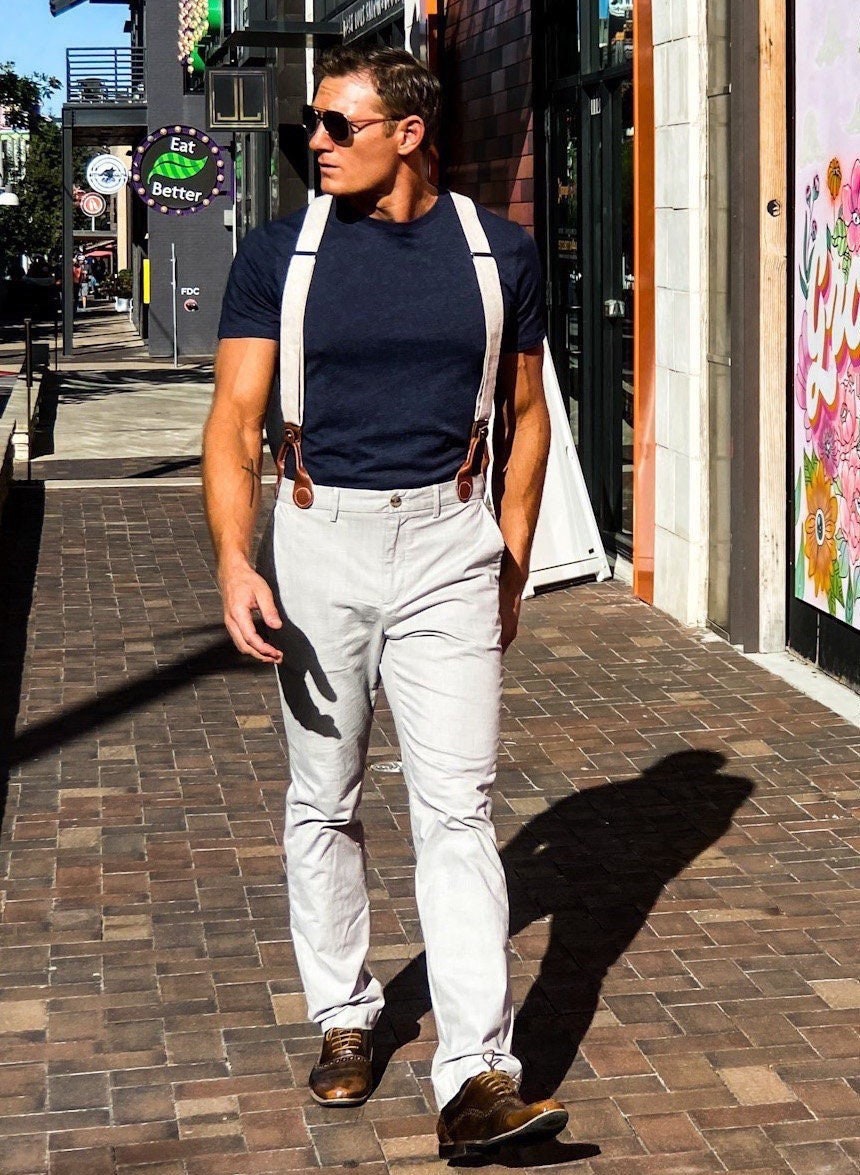 Man walking through The Domain in Austin, Texas, wearing ivory beige linen suspenders with chocolate brown leather attachments. Handmade vintage-style wedding braces paired with modern trousers and a navy shirt.