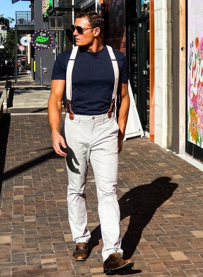 Man walking through The Domain in Austin, Texas, wearing ivory beige linen suspenders with chocolate brown leather attachments. Handmade vintage-style wedding braces paired with modern trousers and a navy shirt.