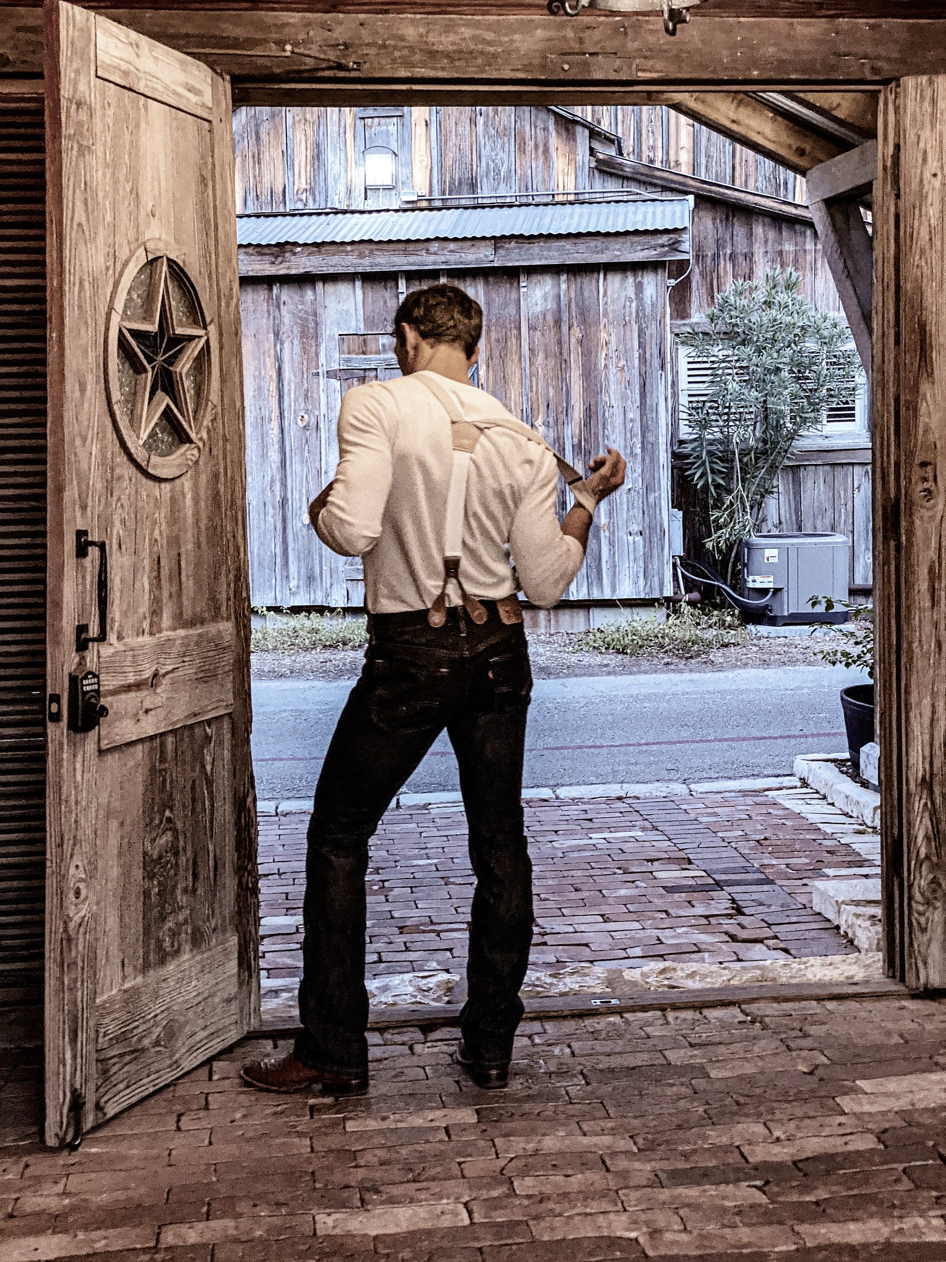 Rustic post-wedding scene featuring ivory beige linen suspenders with leather button-on attachments. Styled with dark denim and a vintage white Henley, this heritage menswear look captures the essence of an Austin, Texas wedding.