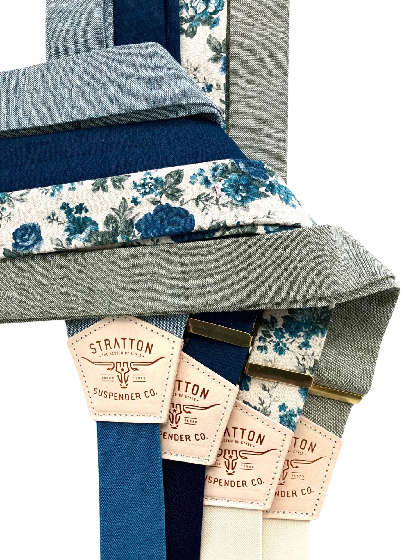 Stacked display of handmade linen suspenders in sky blue, navy, teal floral, and sage gray from Stratton Suspender Co.—designed for weddings, groomsmen, and vintage menswear.